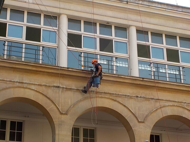 Travaux en hauteur Paris réalisés par cordiste sur façade d’immeuble moderne avec arches et fenêtres vitrées.