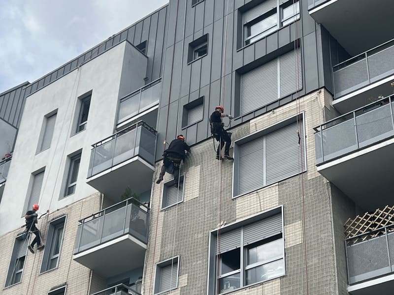 Cordistes réalisant des travaux en hauteur sur la façade d’un immeuble résidentiel moderne à Paris.