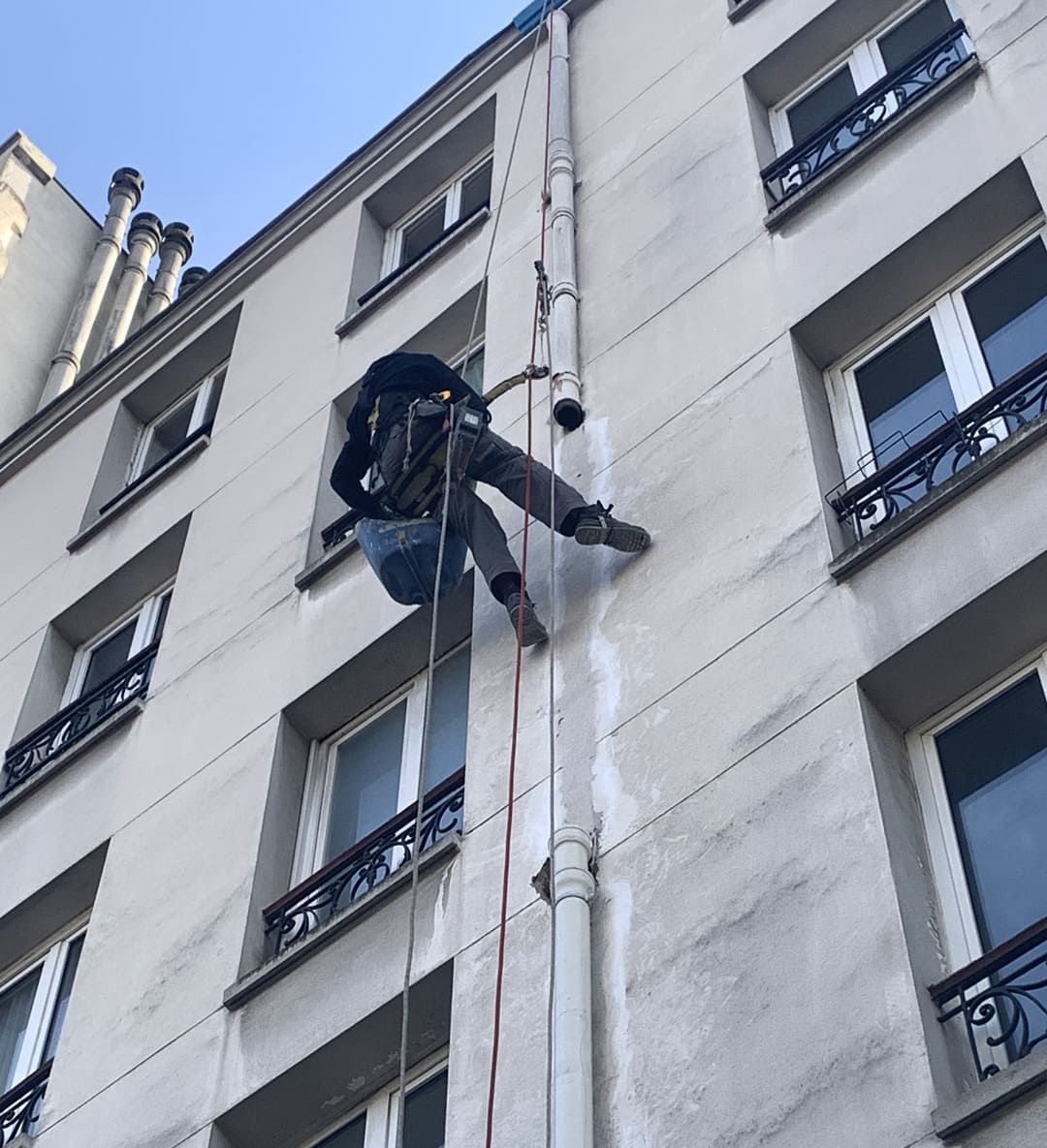 Cordiste effectuant des travaux de réparation de façade en hauteur sur un immeuble à Paris.